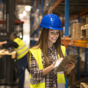 Female warehouse worker holding tablet checking inventory in distribution warehouse.