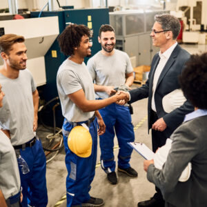 Happy corporate manager shaking hands with black worker after staff meeting in a factory.