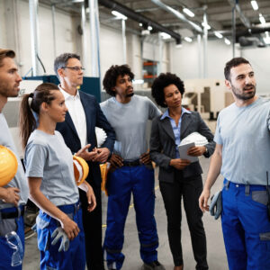 Happy manual worker presenting the results of business development while giving presentation to company leaders and his team in a factory.