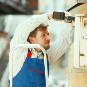 HVAC technician working on a capacitor part for condensing unit. Male worker or repairman in uniform repairing and adjusting conditioning system, diagnosting and looking for technical issues.