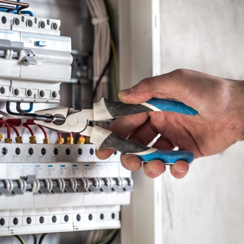 Man, an electrical technician working in a switchboard with fuses. Installation and connection of electrical equipment. Professional with tools in hand. concept of complex work, space for text.